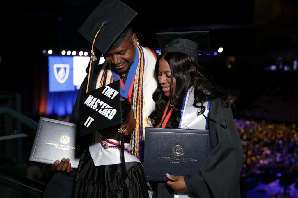 Couple smiling and holding their diploma covers with their son, all wearing cap and gown