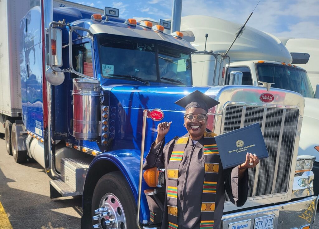Robyn wearing her SNHU regalia standing in front of her semi truck