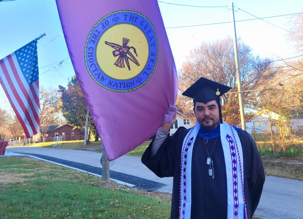 Shane wearing his regalia and holding a flag for the Choctaw Nation 